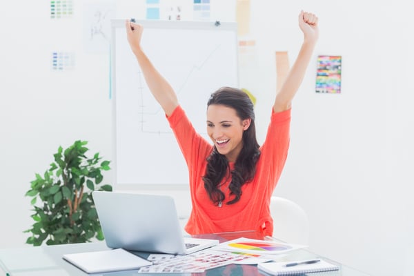 Excited woman raising her arms while working on her laptop in her office