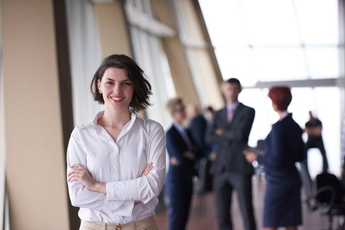 Smilling young business woman in front her team blured in background. Group of young business people. Modern bright  startup office interior.