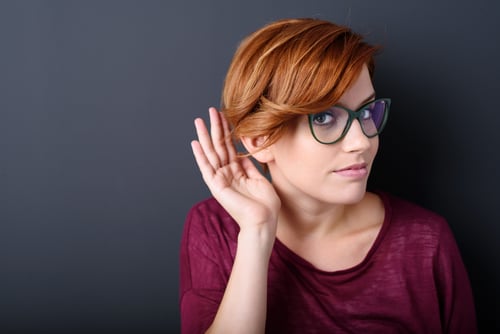 Young woman cupping her hand behind her ear with her head turned aside to listen better